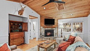 Una sala de estar con chimenea de piedra, techo de madera y un televisor montado.
