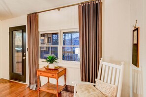 A room with a wooden floor, a white chair, a small table with a plant, a window with curtains, and a door. - Orchid Cabin (Banner Elk)