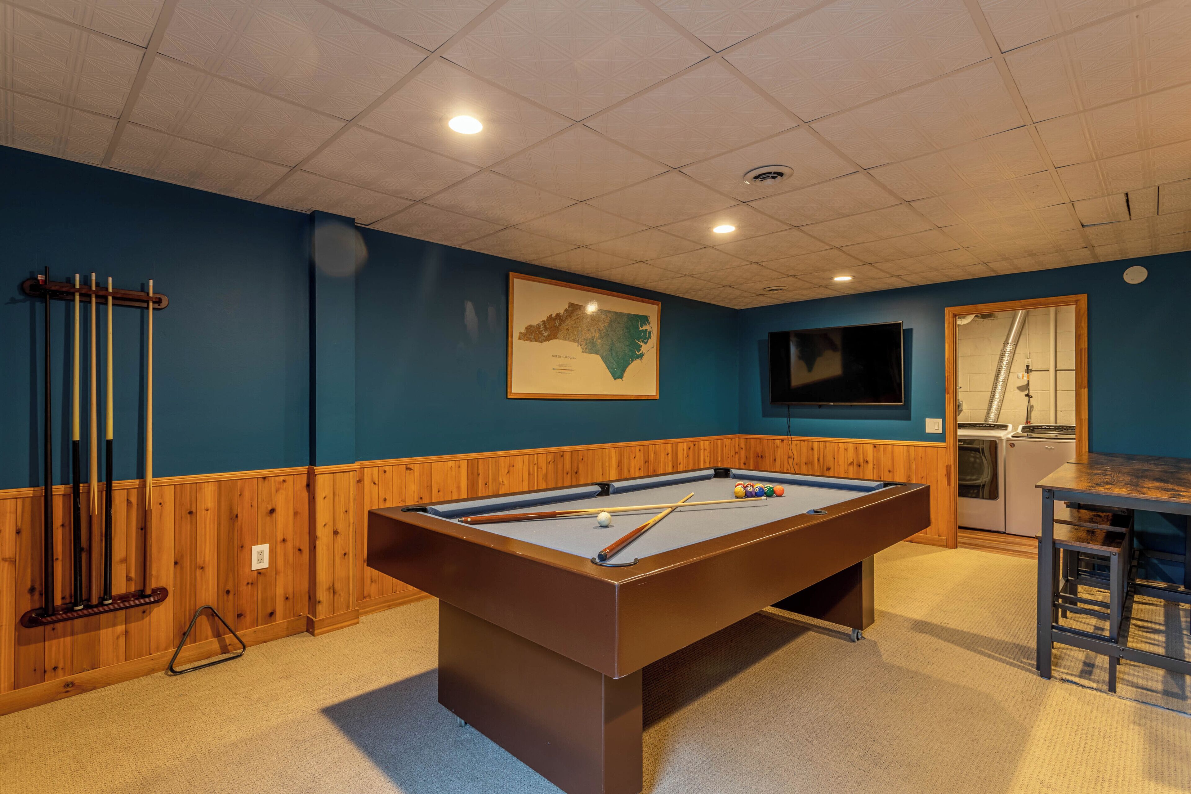 A pool table with surrounding amenities, including a television, a seating area, and a framed map on the wall.