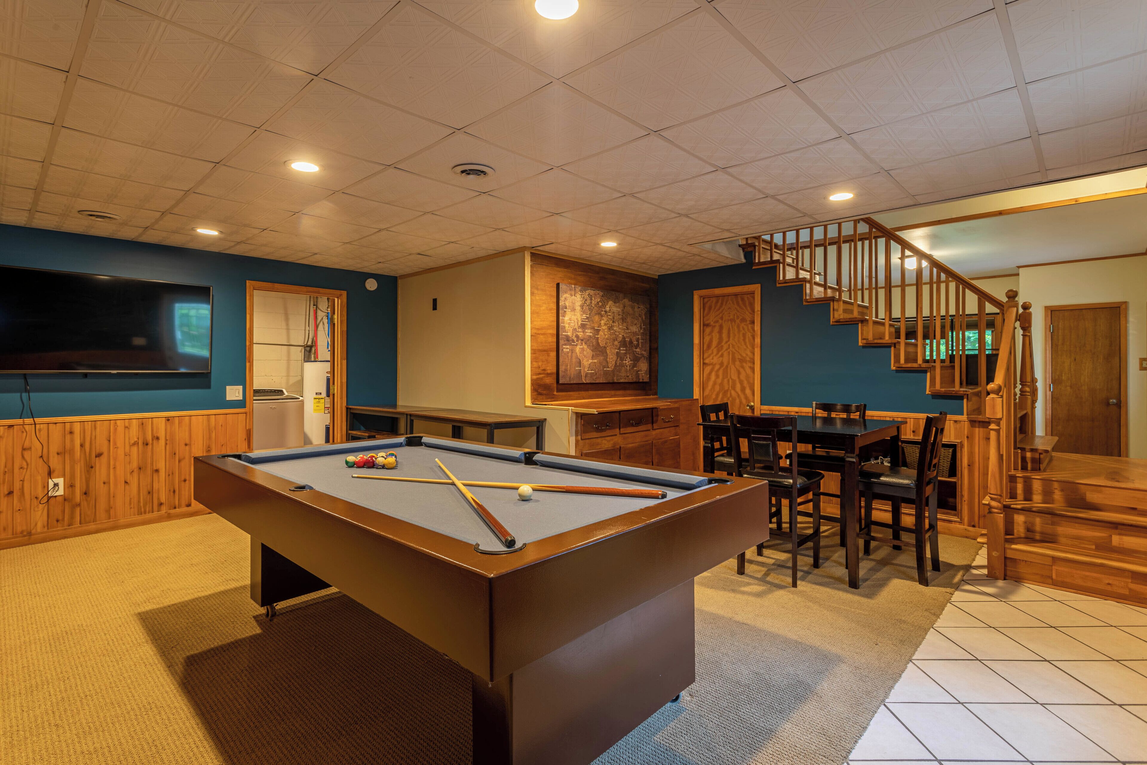 Une table de billard dans une pièce avec un escalier en bois et un coin repas.