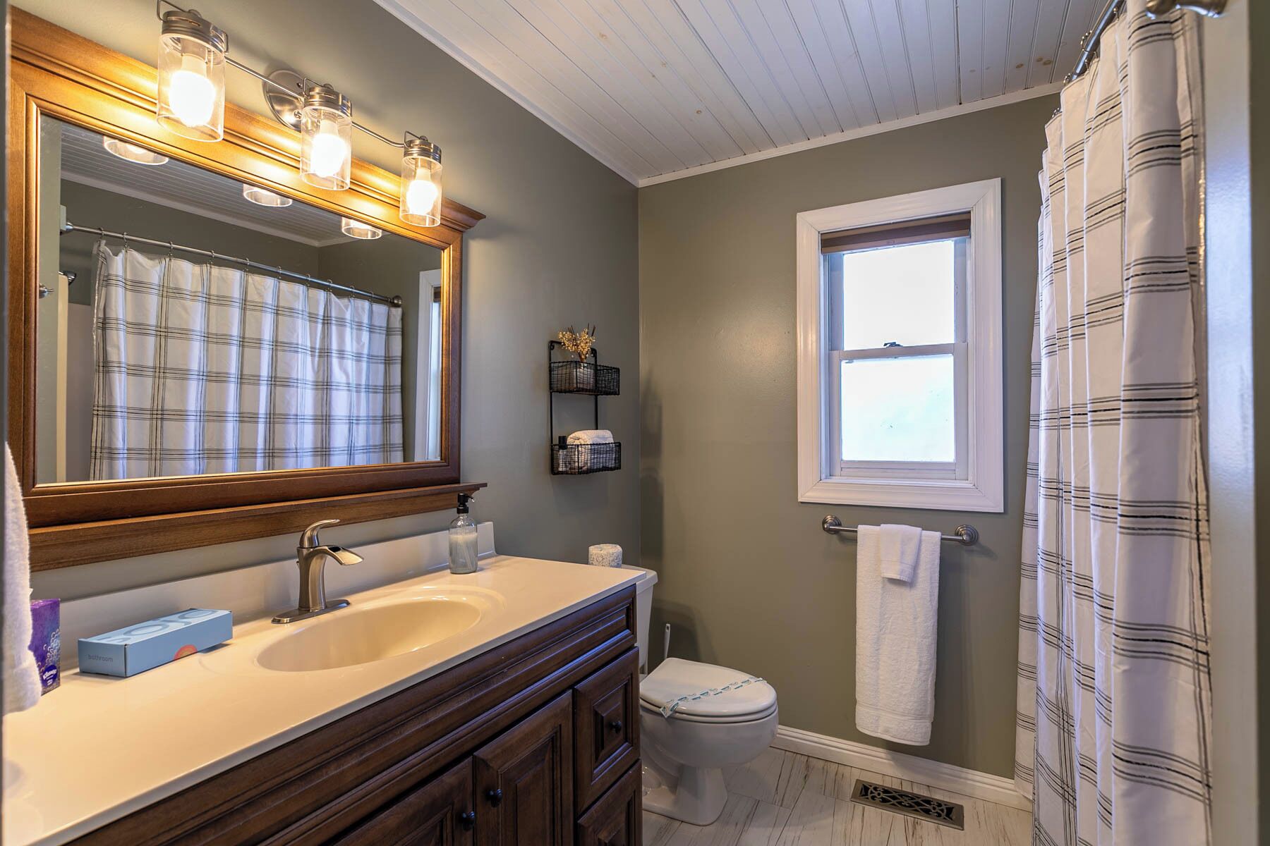 A bathroom with a wooden vanity, a large mirror, a window, and a shower curtain.