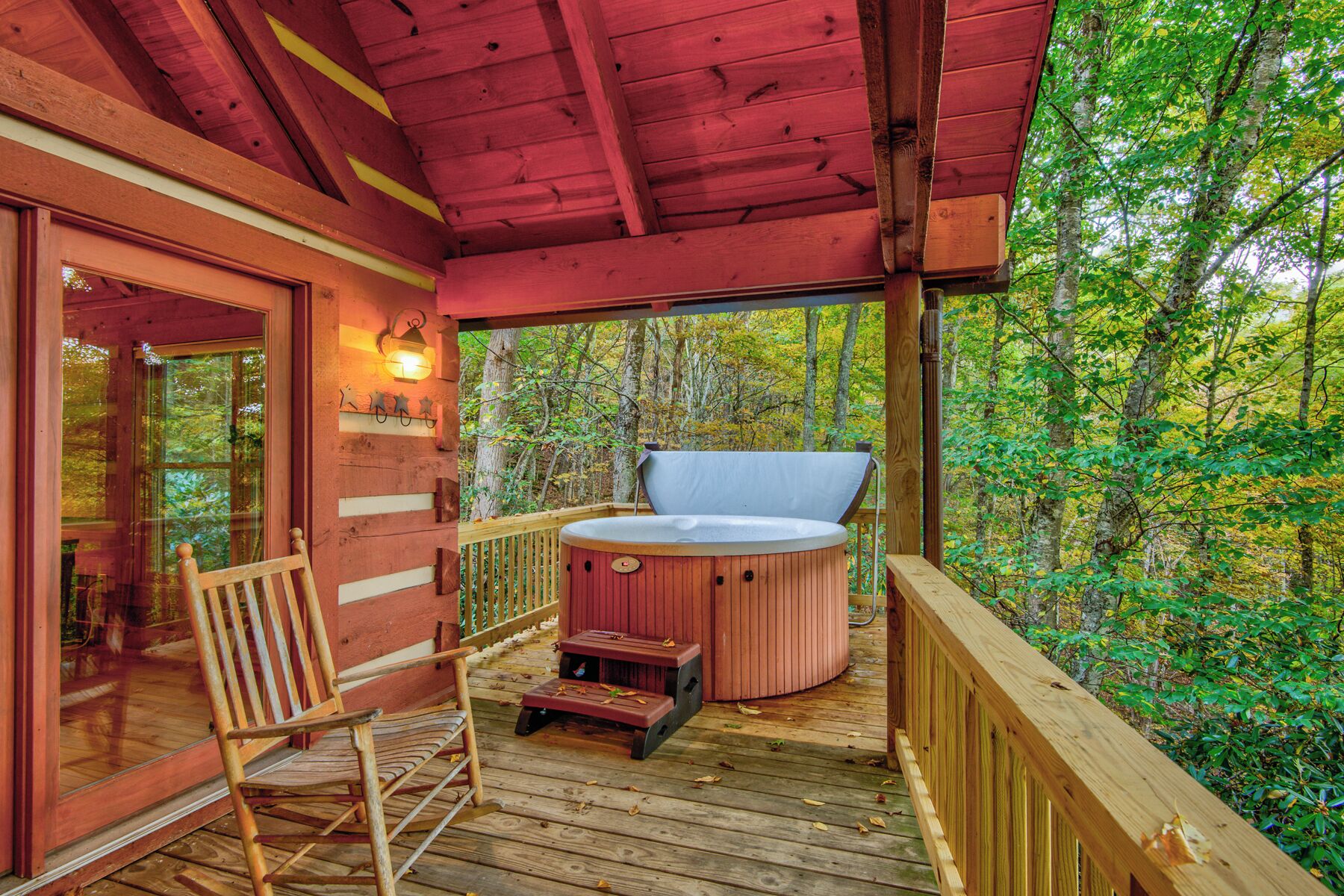 A wooden deck with a hot tub, a chair, and a window overlooking a forest.