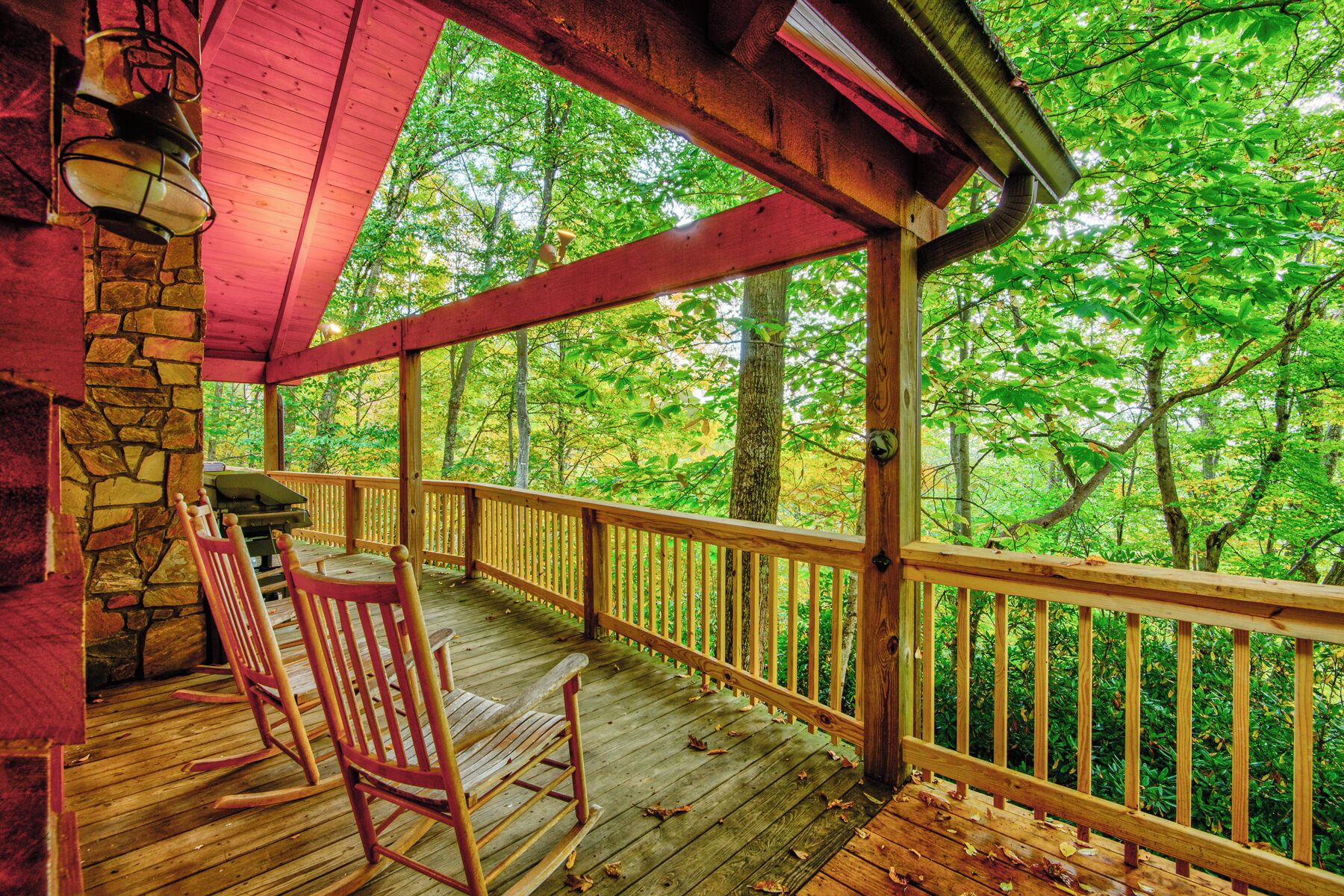 Une terrasse en bois avec un mur en pierre, une chaise berçante et une vue sur une forêt.
