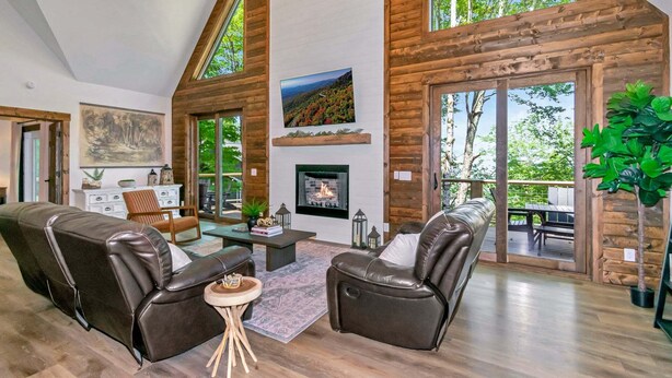 A spacious living room with a fireplace, leather sofas, and large windows. - Beech Blessings - Luxury Spacious Beech Mtn Home With Huge Views (Banner Elk)