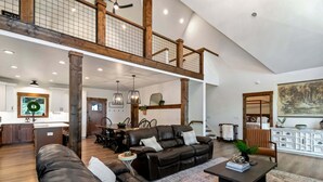 A spacious living area with a high ceiling, a dining area with a wooden table and chairs, and a bedroom with a large bed and a painting. - Beech Blessings - Luxury Spacious Beech Mtn Home With Huge Views (Banner Elk)