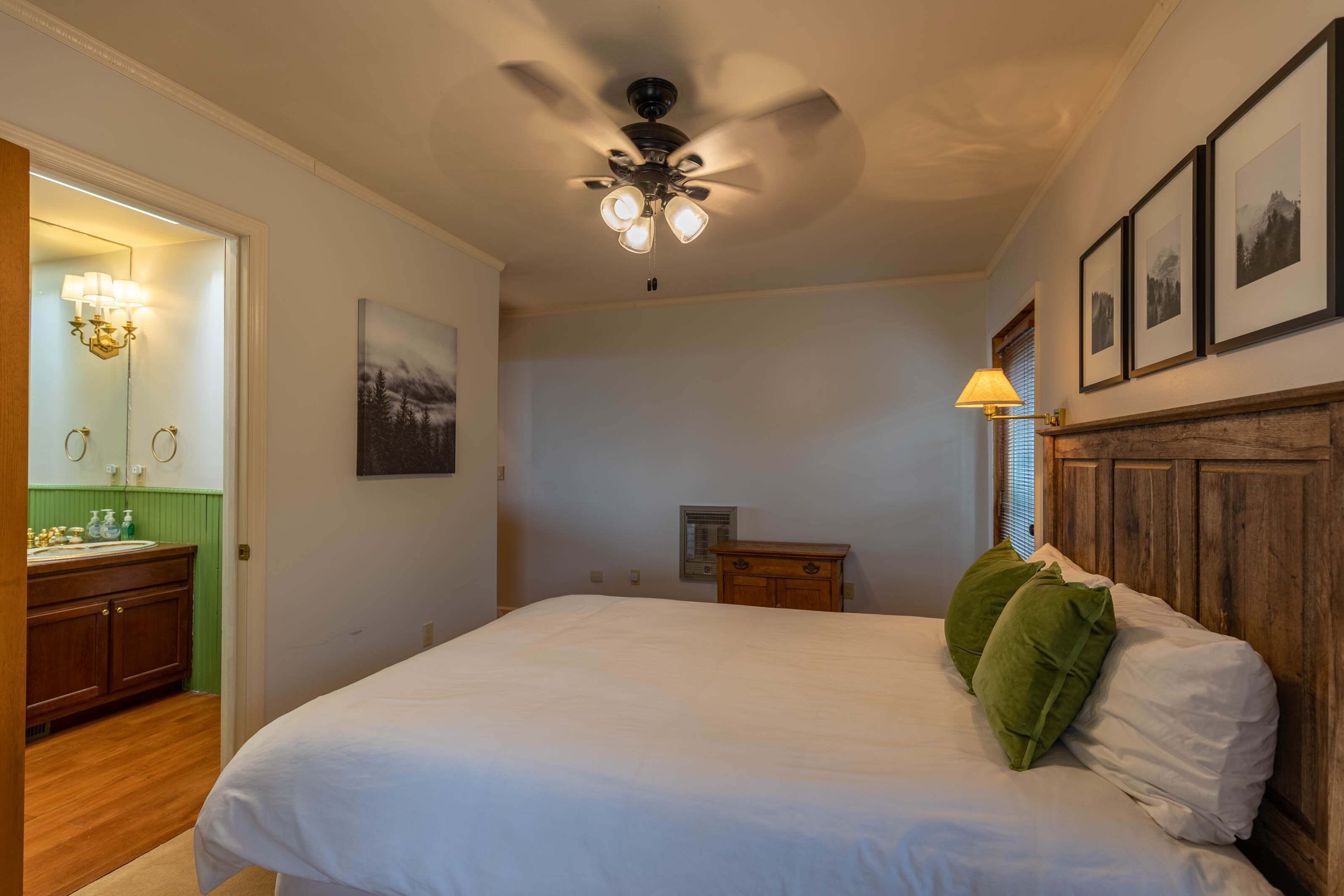 A bedroom with a bed, a ceiling fan, a nightstand, a dresser, and framed pictures on the wall.