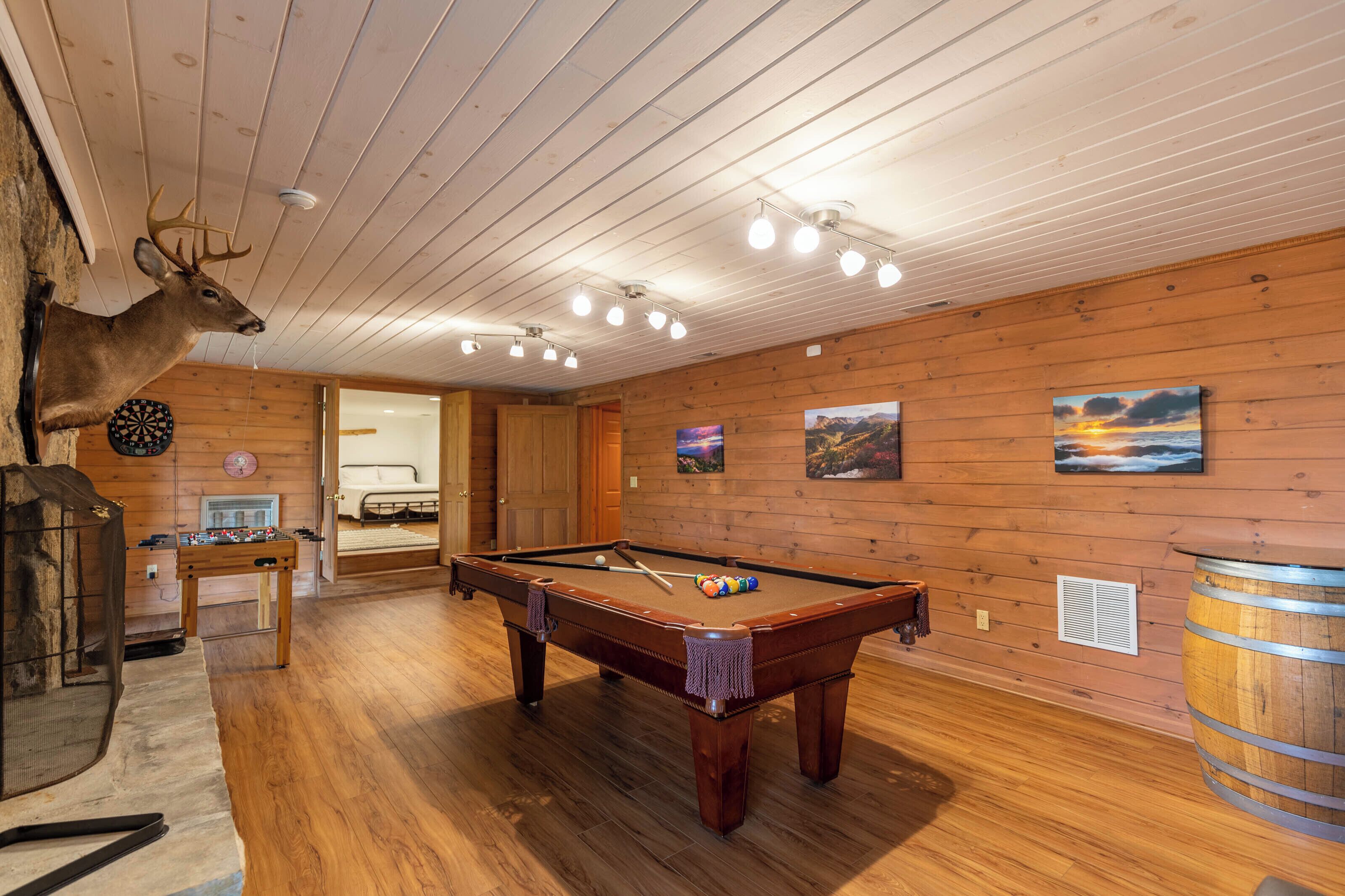 A wooden-paneled room with a pool table, a dartboard, and a mounted deer head.