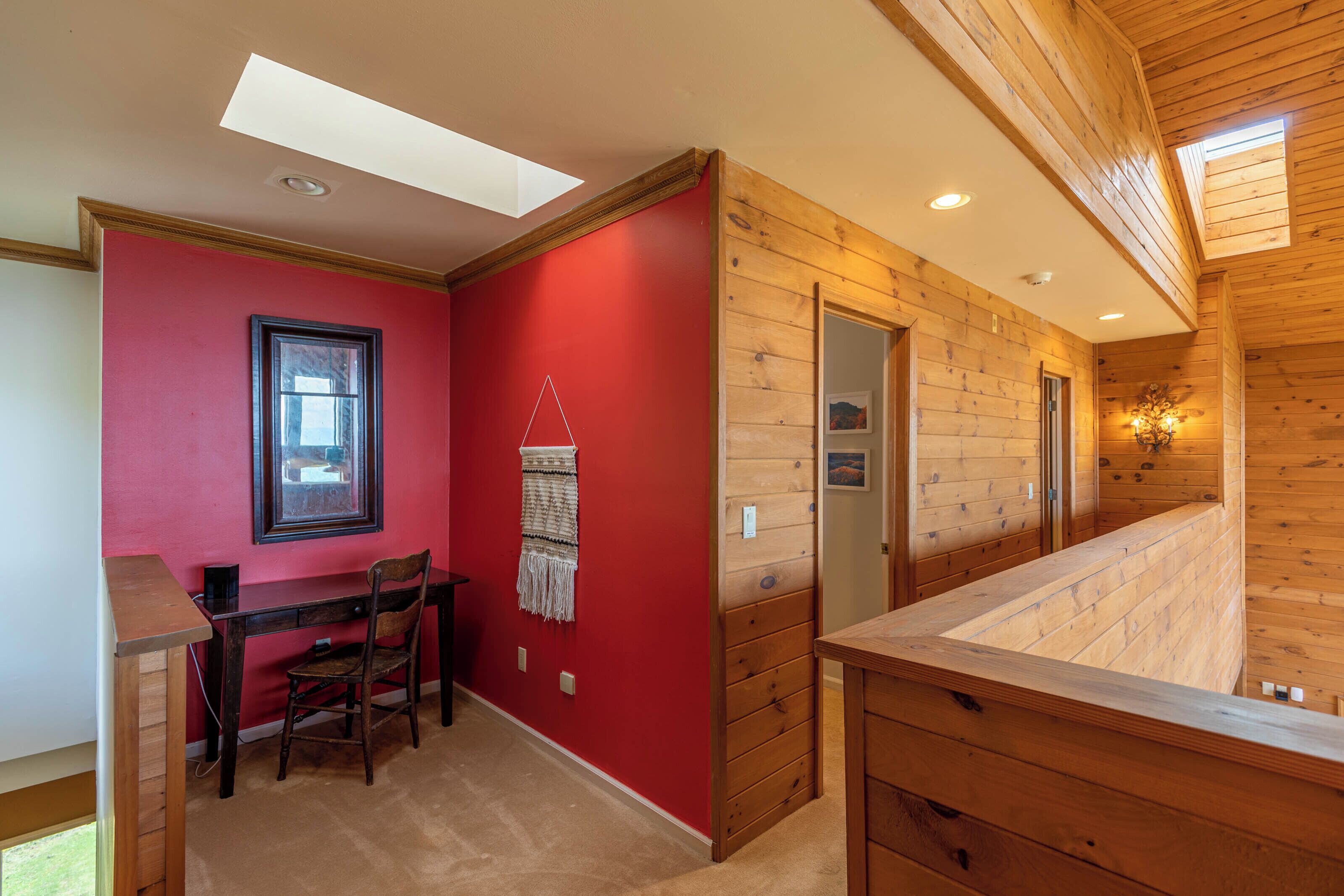 A room with a red wall, wooden ceiling, and a desk with a chair.