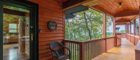 A wooden cabin with a porch, a chair, and a view of trees.