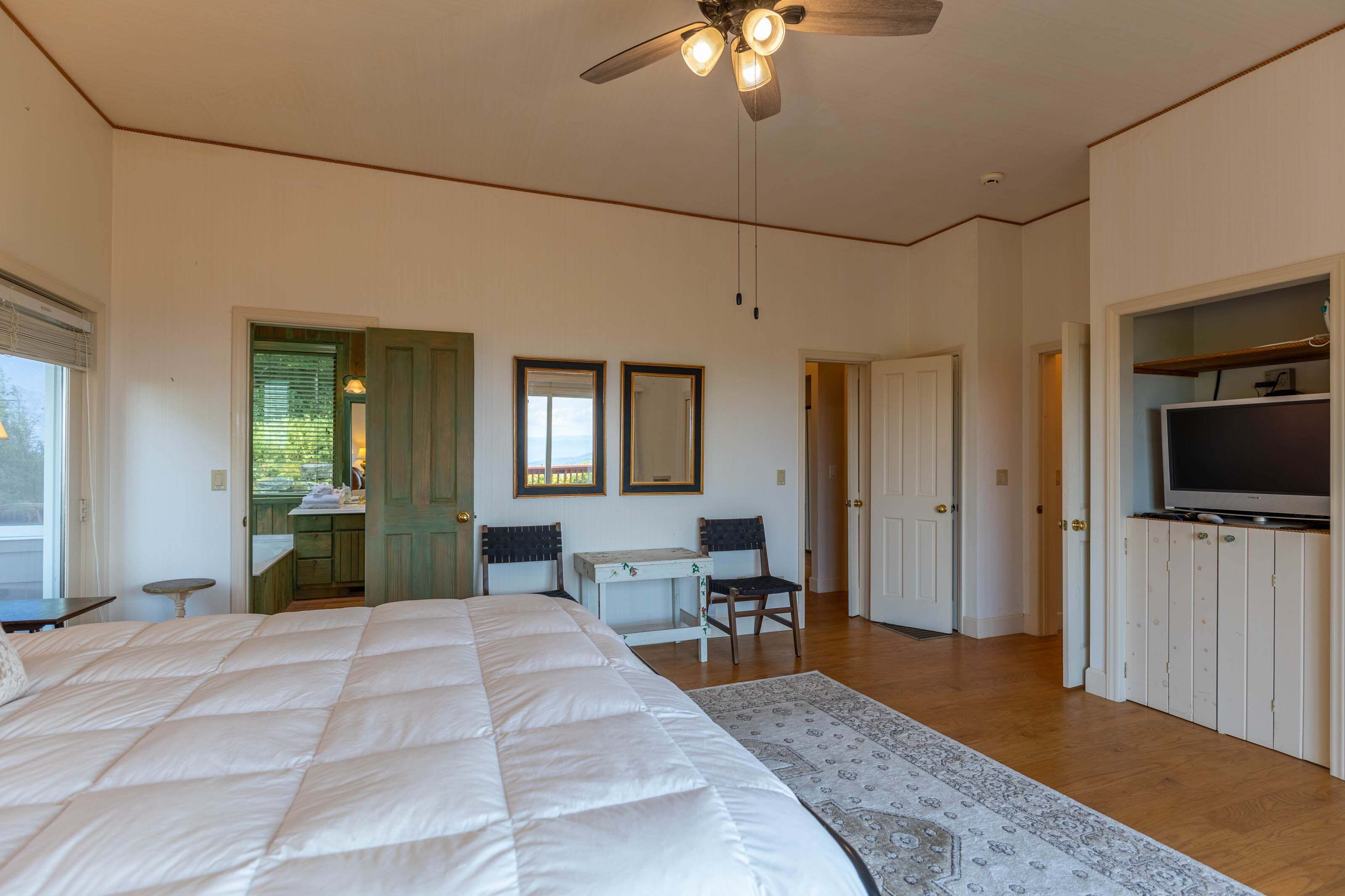 A bedroom with a bed, a desk, a chair, a TV, and a ceiling fan.