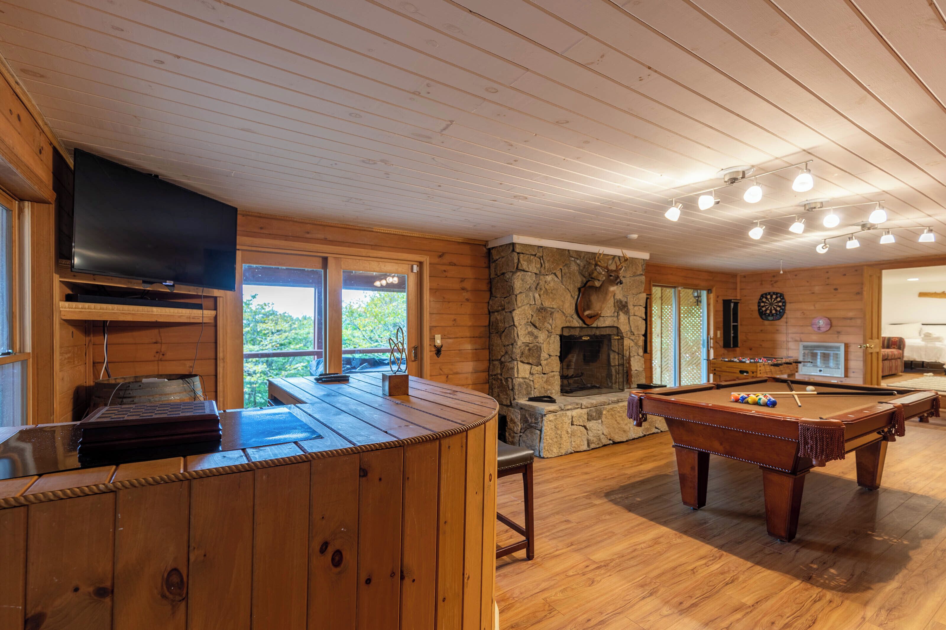 A wooden interior with a pool table, a fireplace, and a television.