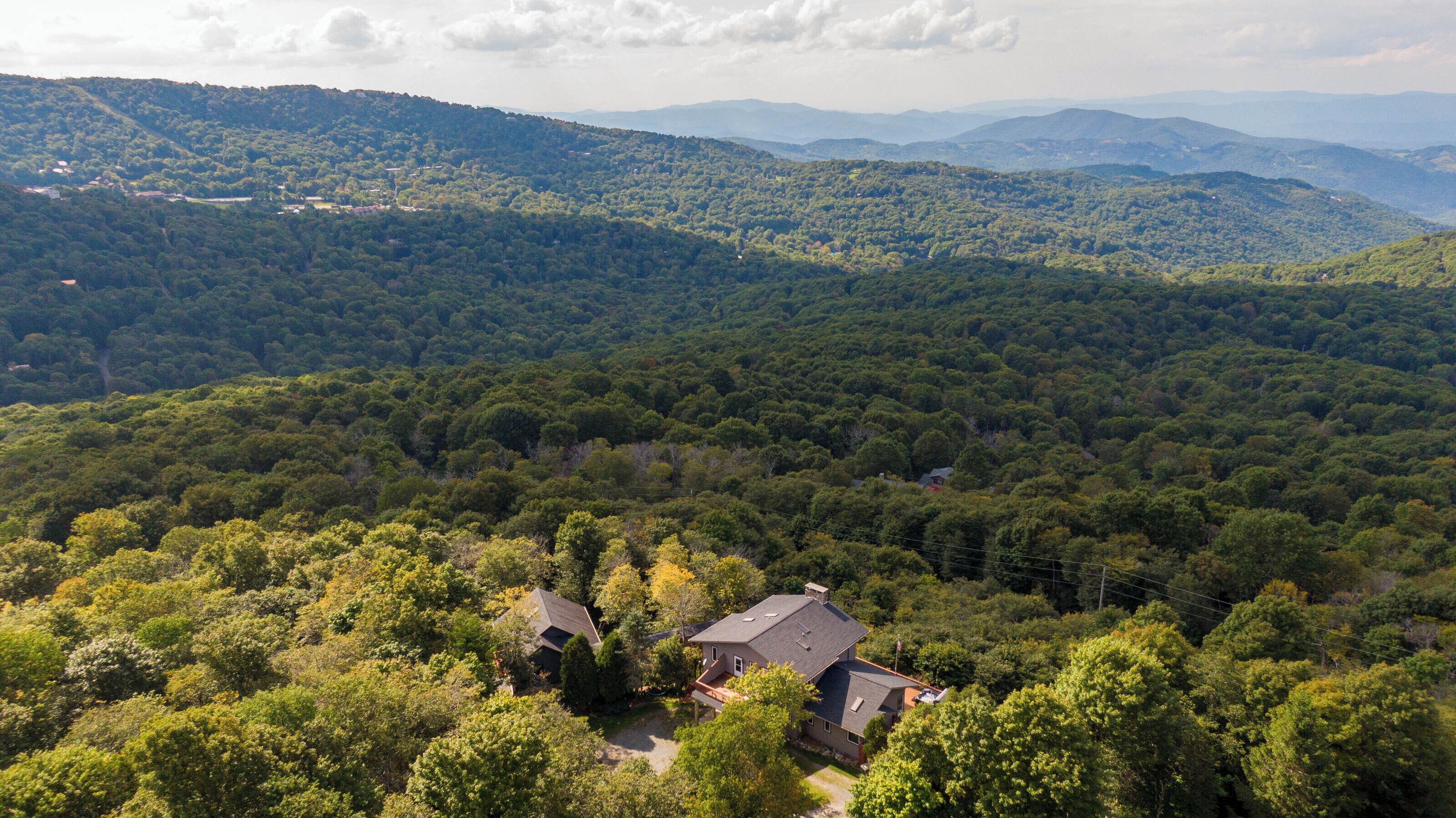 A house surrounded by dense forest with a clear view of distant mountains.