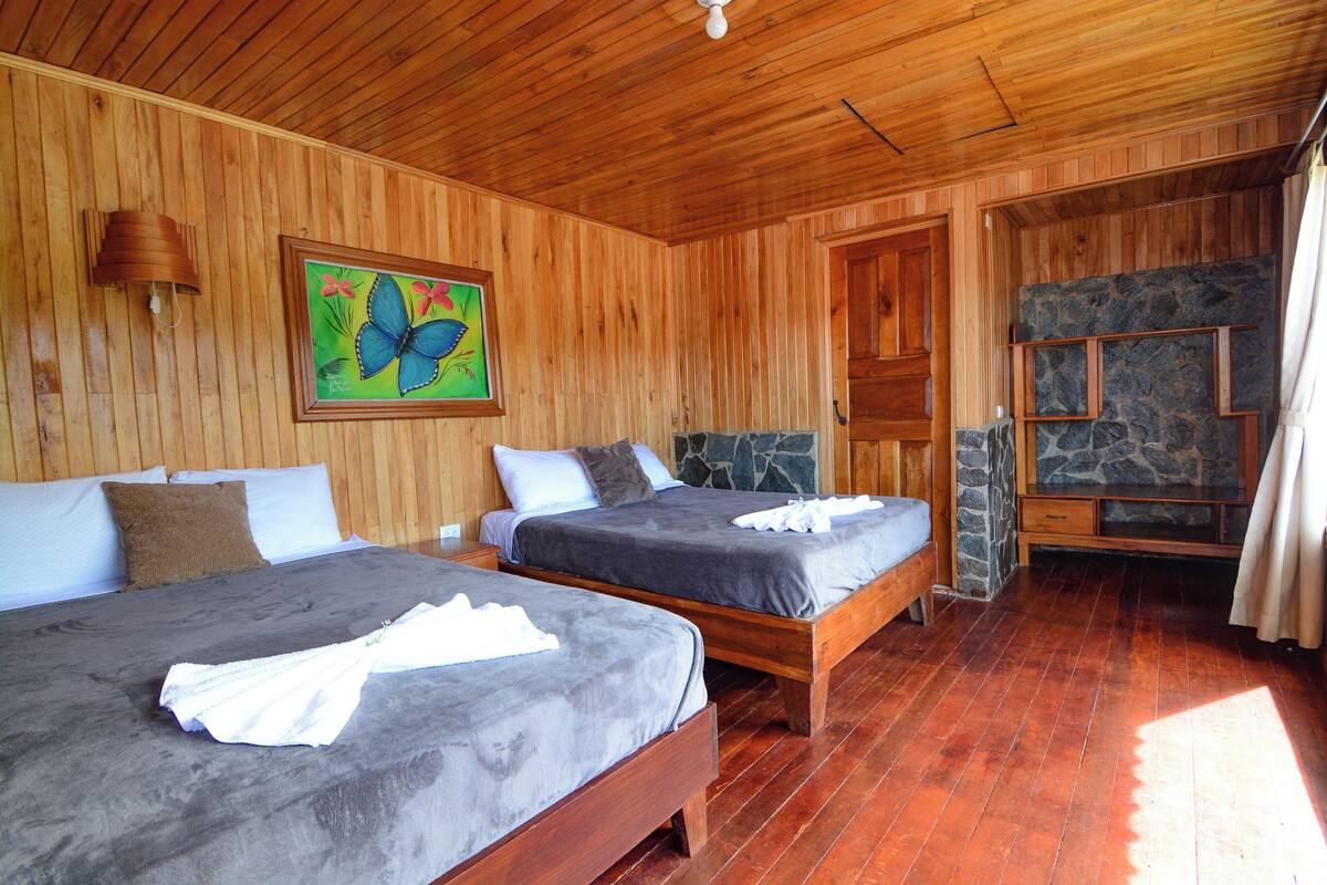 Una habitación de madera con dos camas, una chimenea de piedra y un cuadro de una mariposa.
