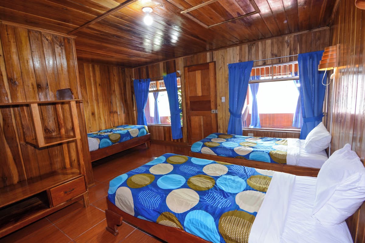 Interior de madera con dos camas, un armario de madera y una ventana con cortinas.