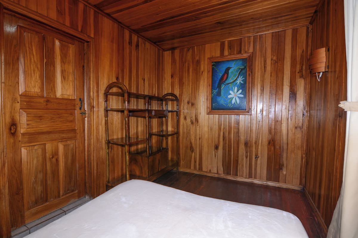 Una habitación con paneles de madera, una cama, una estantería y un cuadro en la pared.