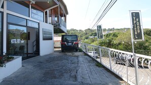 Un hotel con un letrero que anuncia servicios de tours y transporte, un automóvil estacionado al frente y vistas de la vegetación circundante.