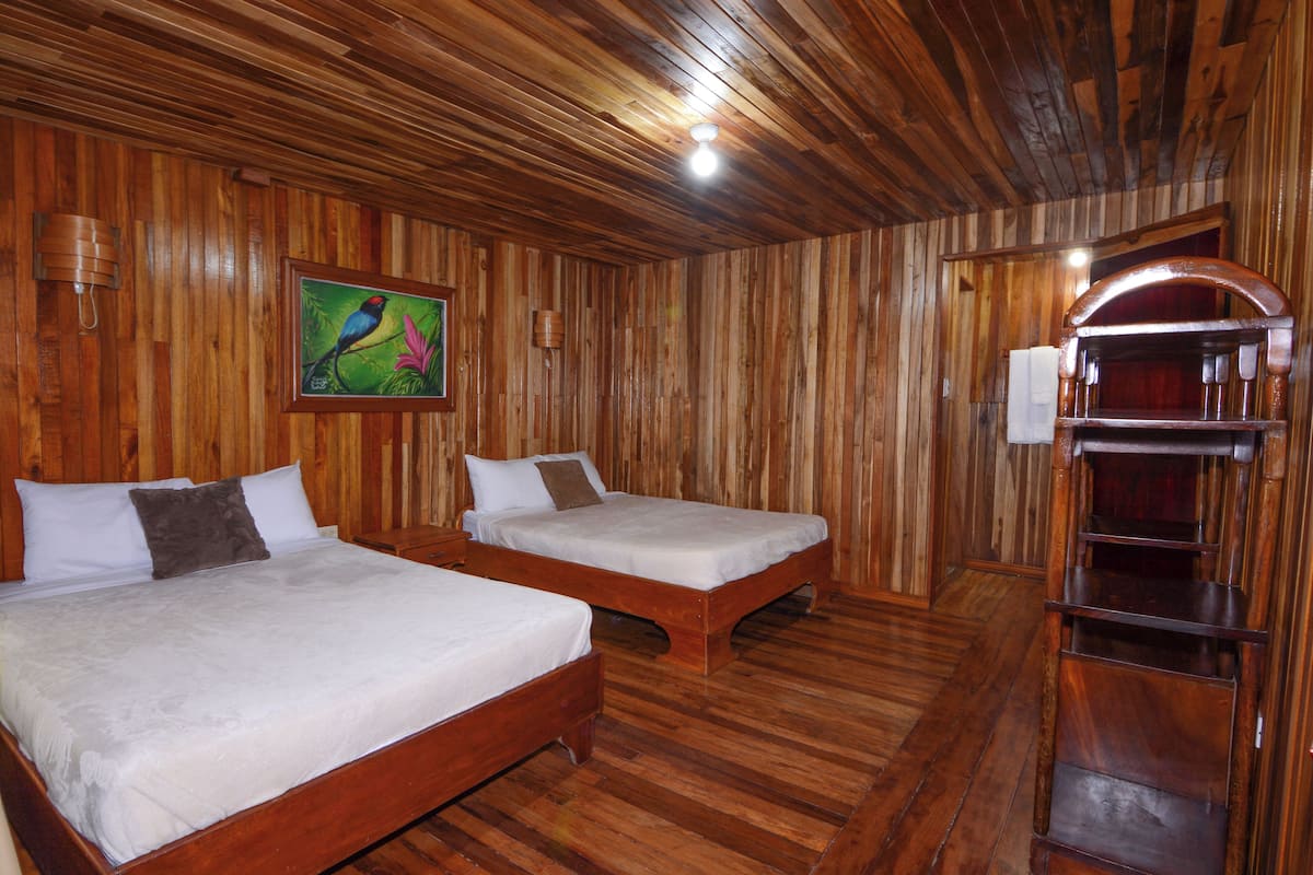 Una habitación con paneles de madera, dos camas, un cuadro y un estante de madera.