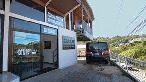 Un hotel con un cartel de servicios de tours y transporte, una entrada de vidrio y un vehículo estacionado afuera.