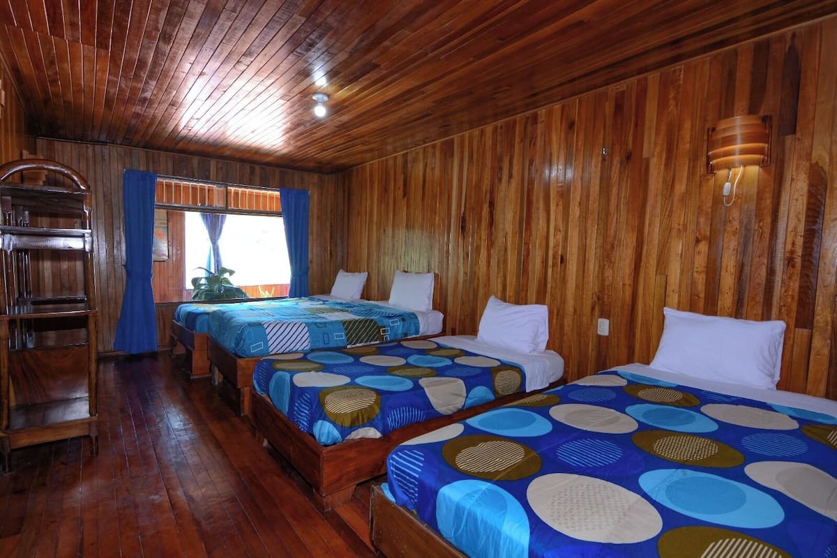 Una cabaña de madera con tres camas, un banco de madera y una ventana con cortinas.