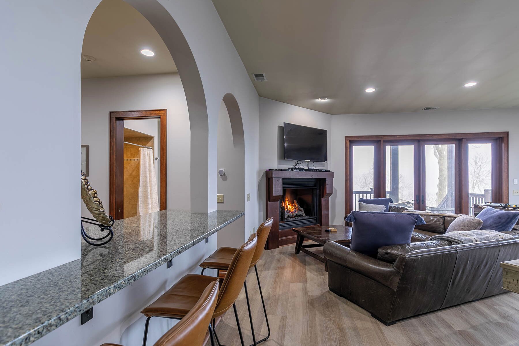 A spacious living room with a fireplace, a large TV mounted above it, and a comfortable seating area with a sofa and chairs.