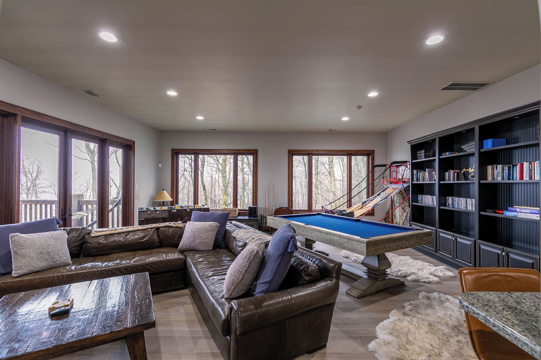 A spacious living room with a pool table, leather sofa, and a bookshelf.