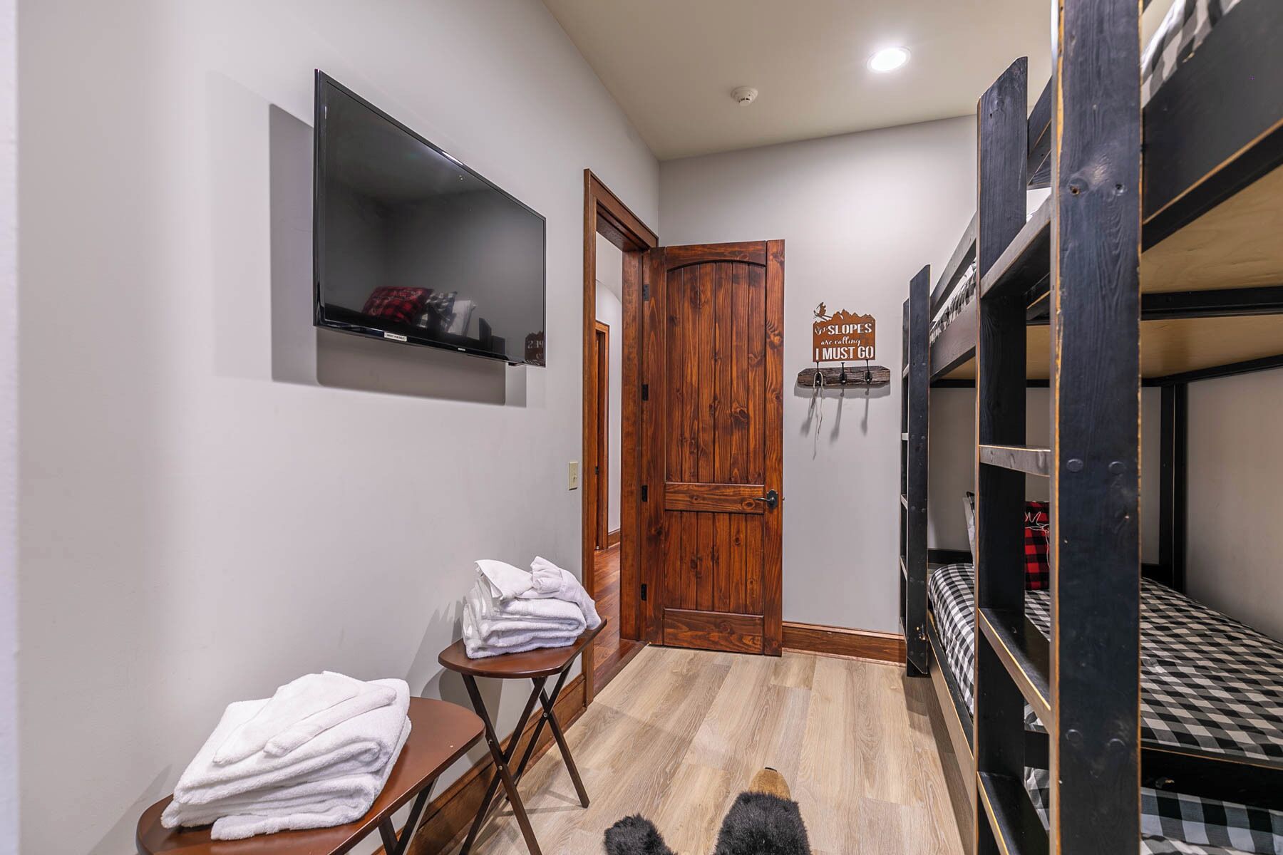 Una habitación pequeña con literas, una mesita con toallas, un estante con objetos y una puerta de madera.
