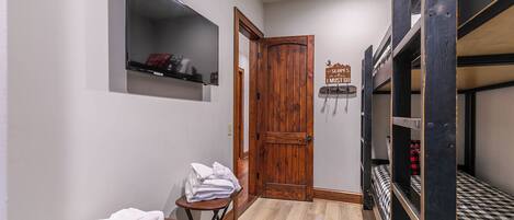 Una habitación pequeña con literas, una mesita con toallas, un estante con objetos y una puerta de madera.