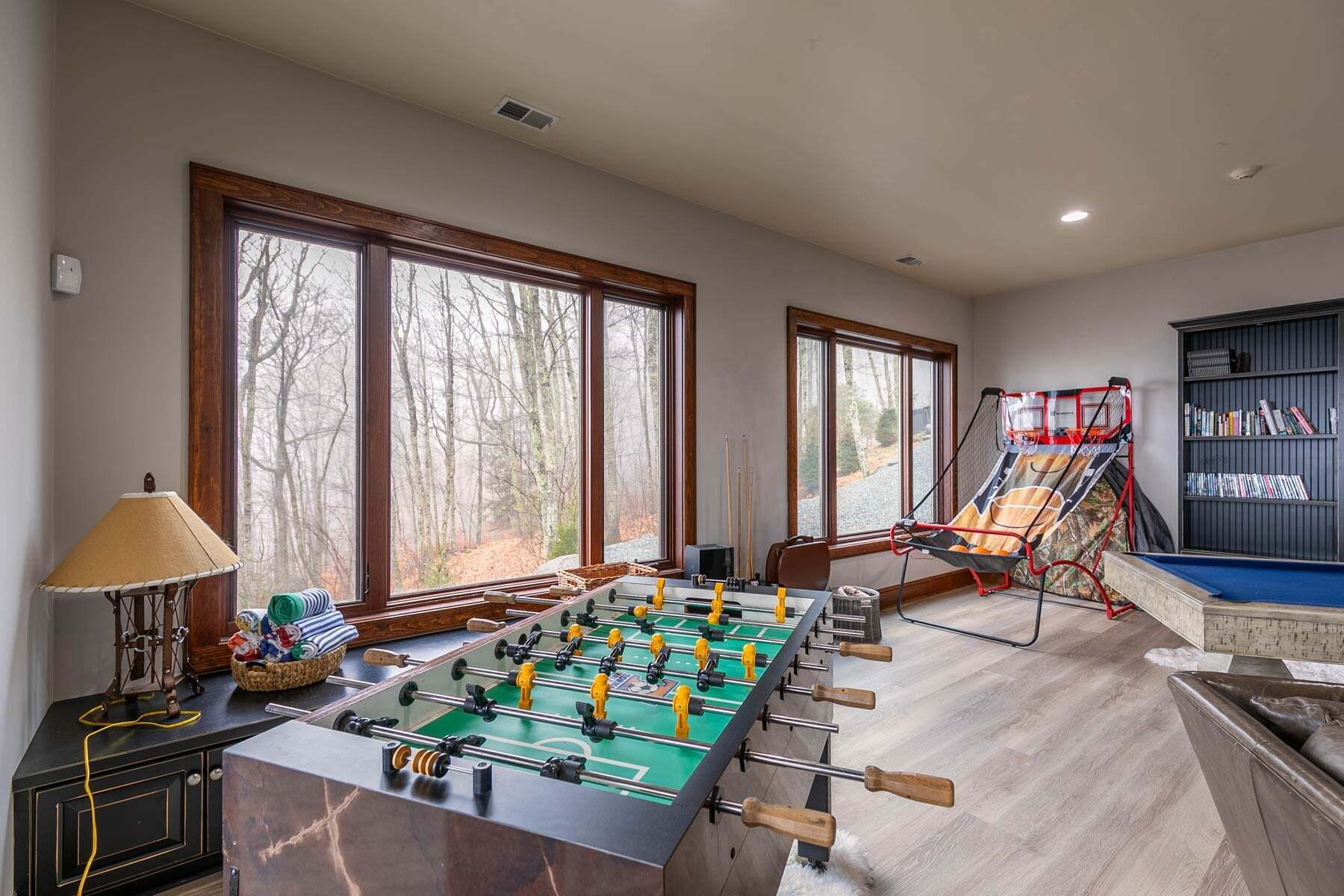 A room with a foosball table, a bookshelf, and large windows.
