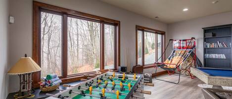A room with a foosball table, a bookshelf, and large windows.