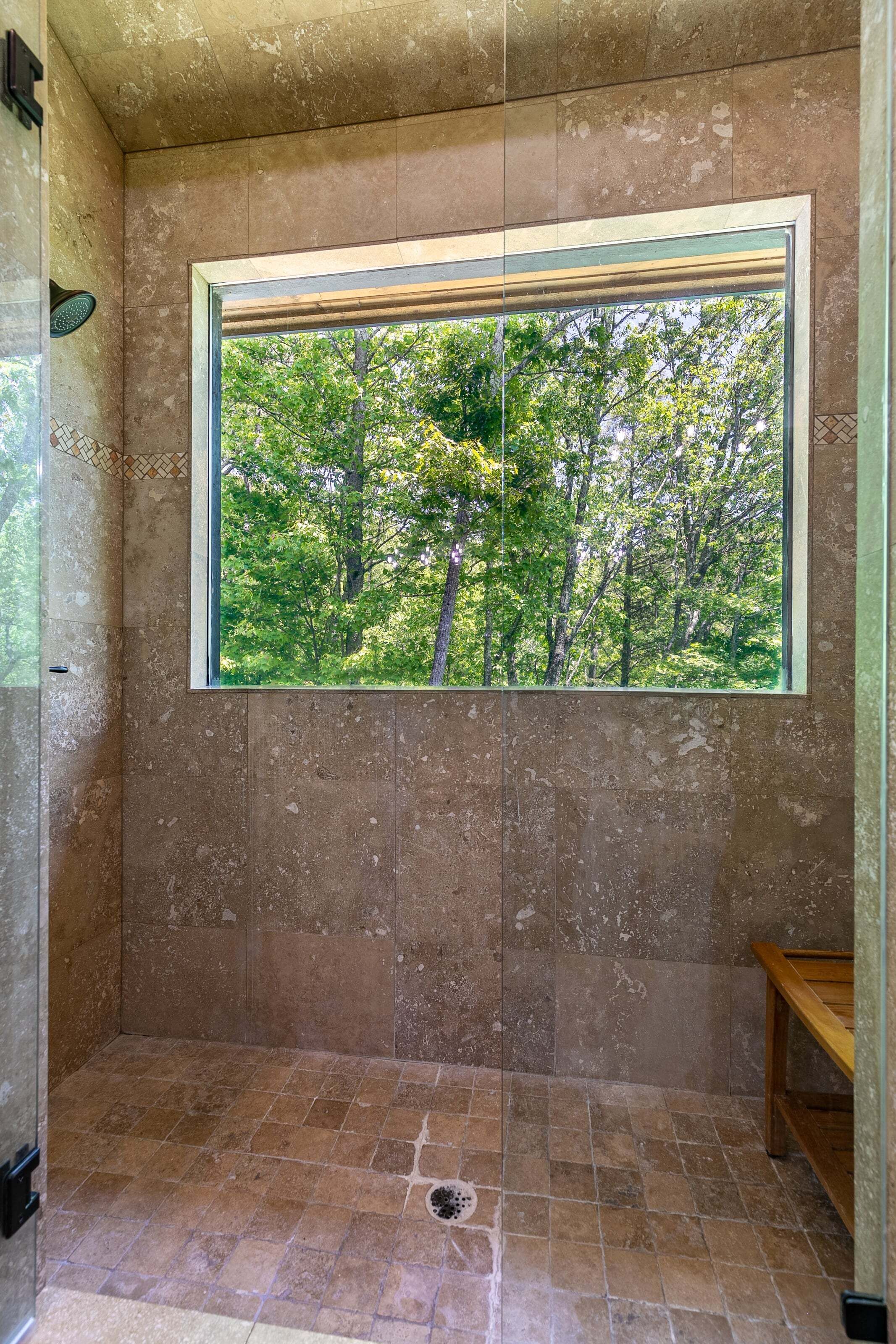 A bathroom with a large window, tiled walls, and a shower area.