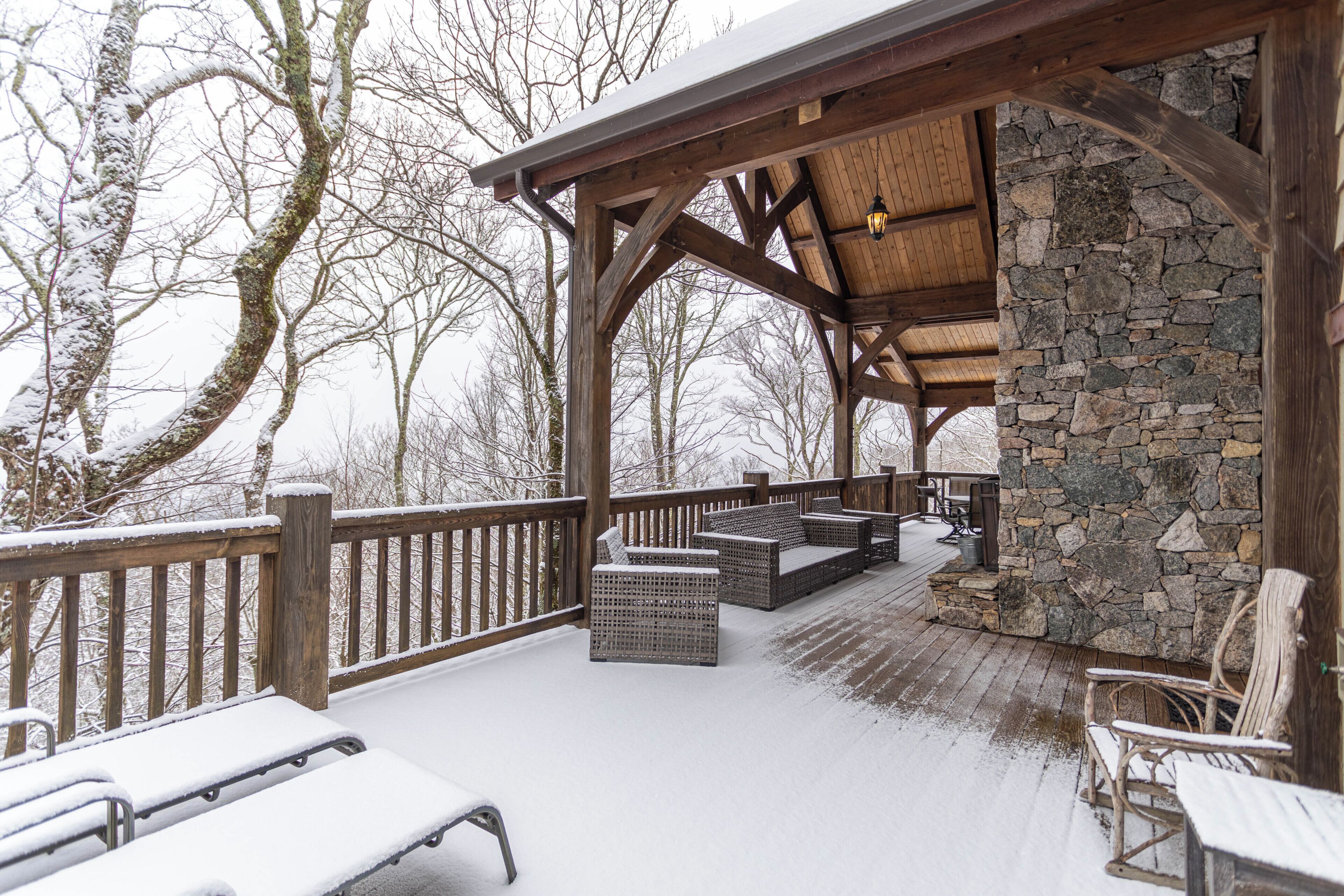 A covered outdoor seating area with stone walls and wooden beams, featuring benches and chairs.