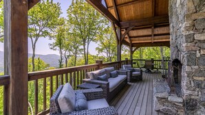A covered outdoor seating area with wicker furniture and a stone fireplace. - Sanctuary at Eagles Nest (Banner Elk)