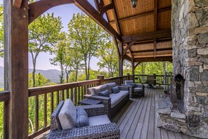 A covered outdoor seating area with wicker furniture and a stone fireplace. - Sanctuary at Eagles Nest (Banner Elk)