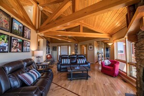 A spacious living area with a high ceiling, wooden beams, leather sofas, a red armchair, and a stone wall. - A Nest With a View (Blowing Rock)