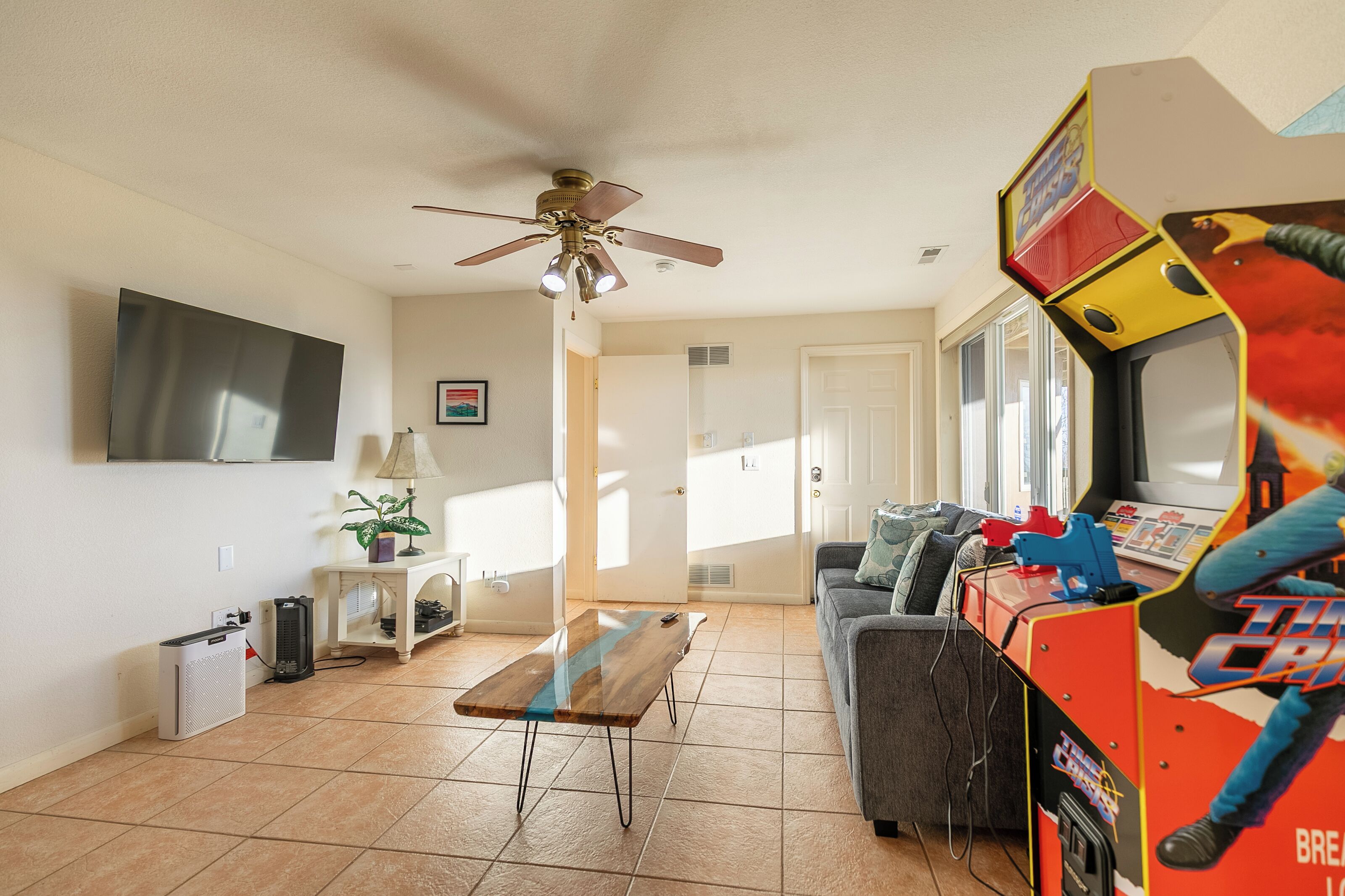 A living room with a ceiling fan, a TV, a sofa, a coffee table, and a gaming machine.