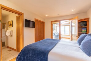 Ein Schlafzimmer mit Bett, Fernseher, Holzschrank und einer Tür, die auf einen Balkon führt.