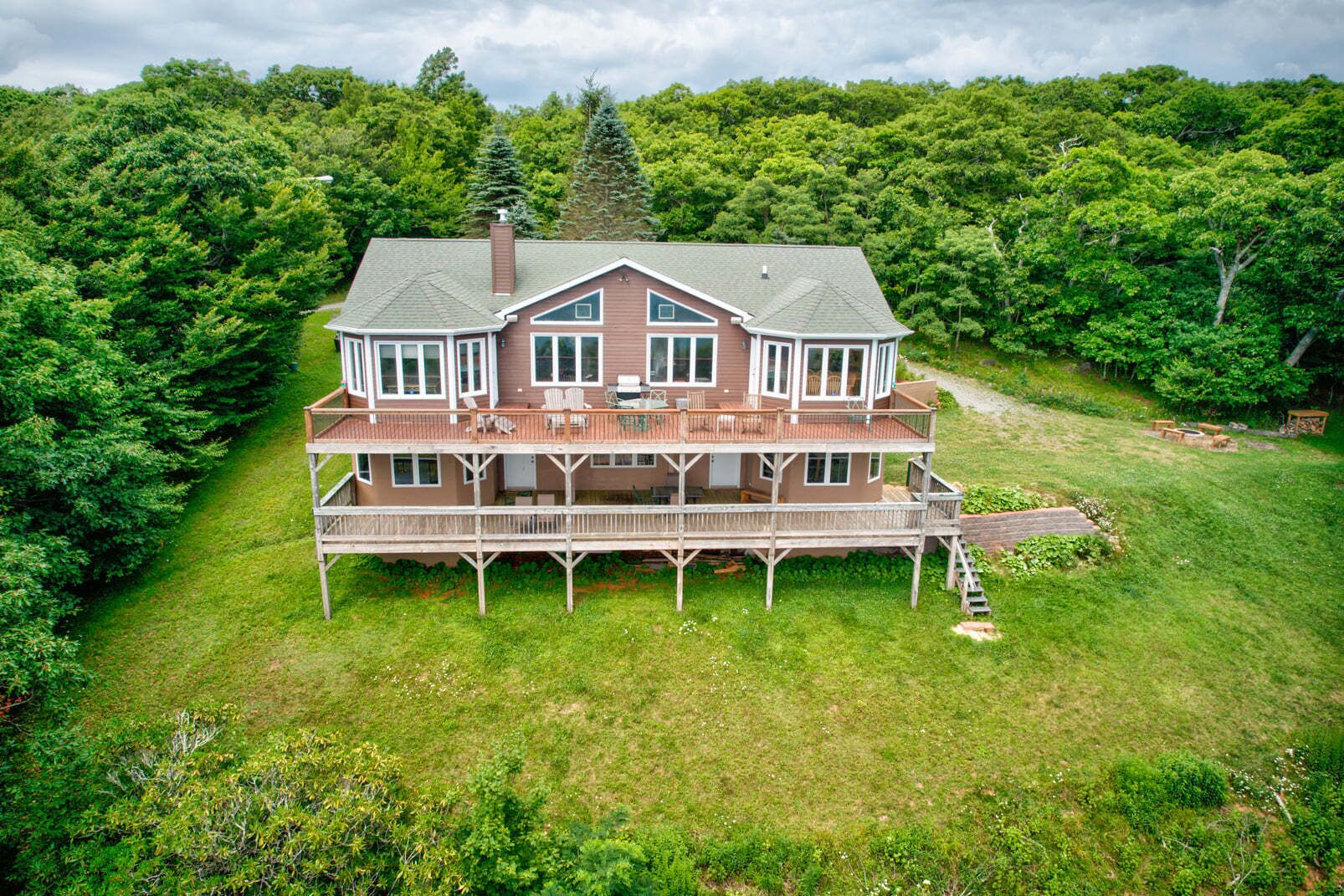 A two-story house with a deck, surrounded by lush greenery.