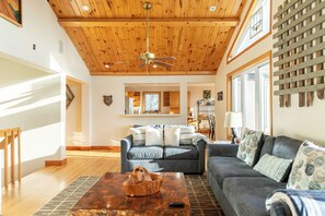 Ein geräumiges Wohnzimmer mit Deckenventilator, Holzboden, grauem Sofa und Couchtisch.
