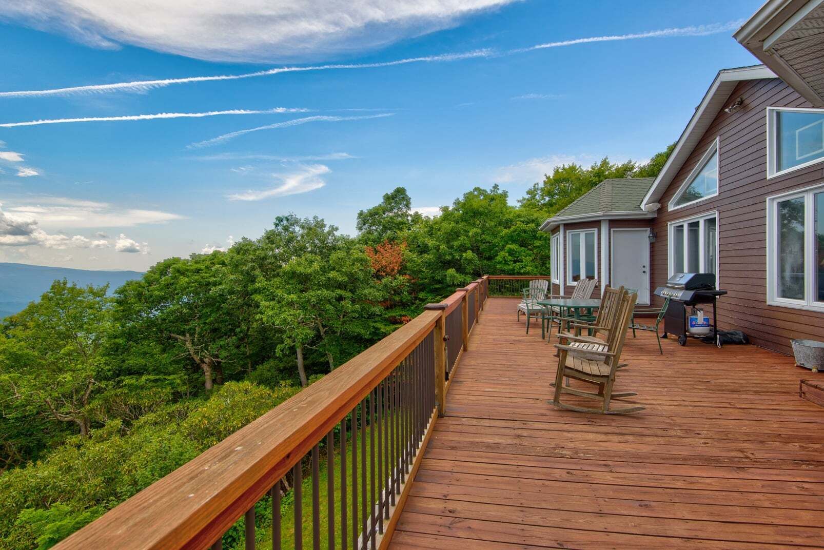 A wooden deck with outdoor furniture, a grill, and a view of the ocean.