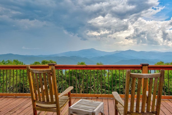Eine Holzdar Terrasse mit zwei Stühlen und einem Tisch, mit Blick auf eine gebirgige Landschaft.