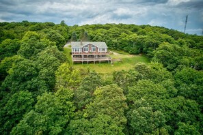 Ein großes Haus, umgeben von dichtem Wald, mit einer sichtbaren Terrasse und einer Treppe, die zum Haupteingang führt.