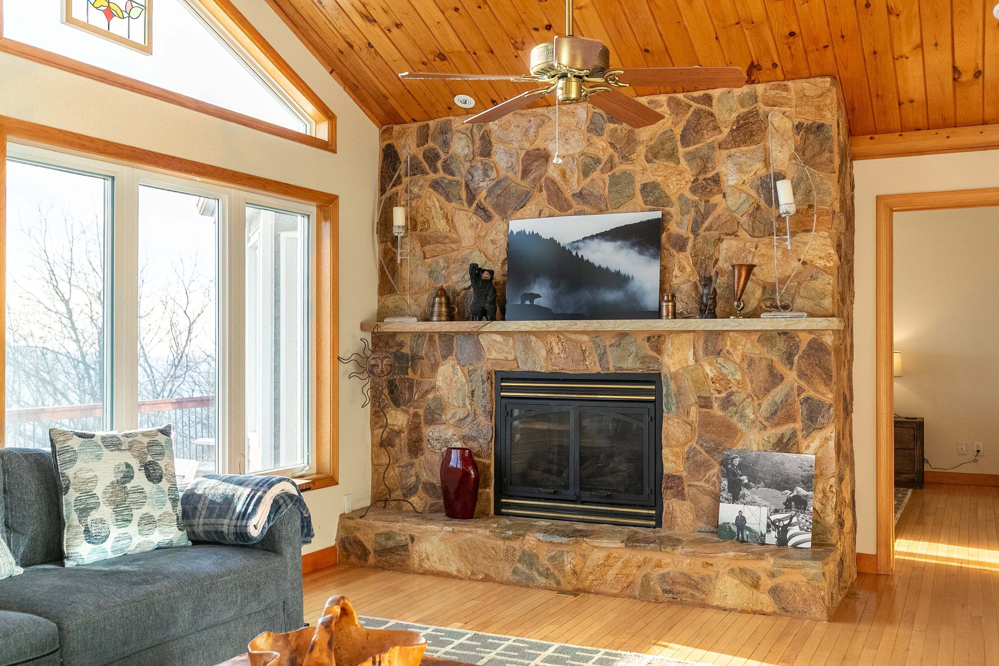 A stone fireplace with a framed picture, a sofa with patterned cushions, and a ceiling fan.