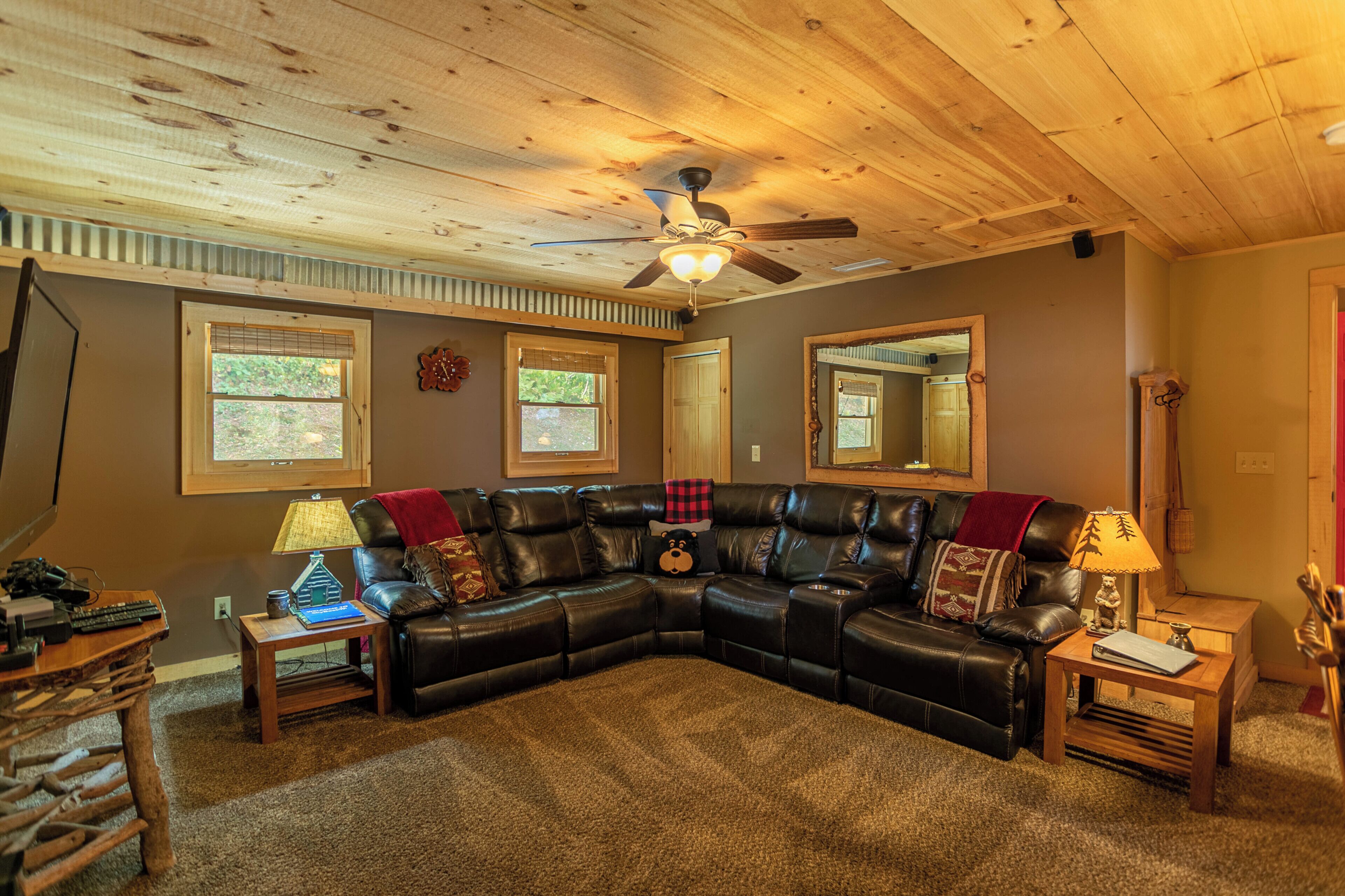 A living room with a sectional sofa, a ceiling fan, and a wooden ceiling.
