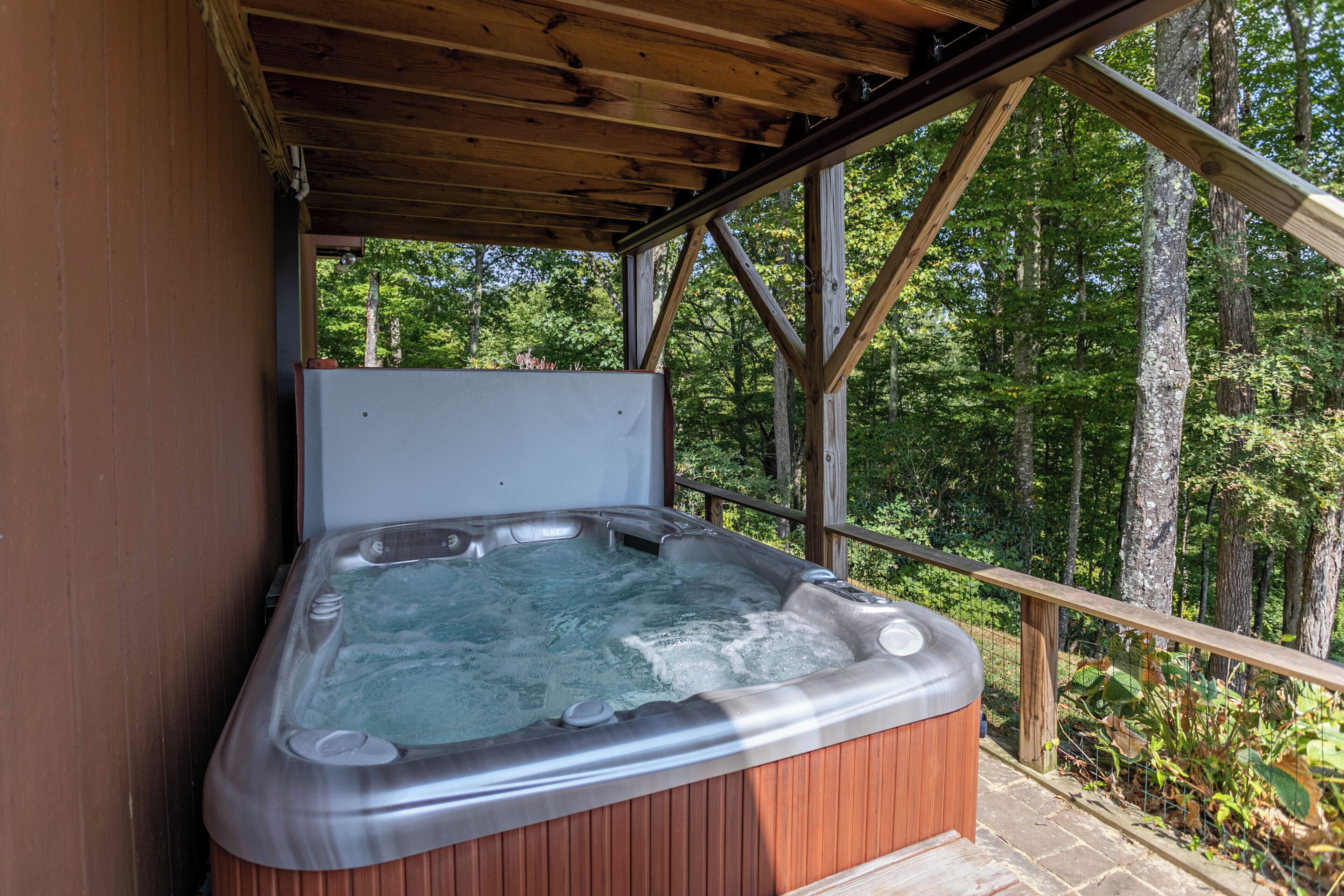 A hot tub in a wooden structure with a view of a forest.
