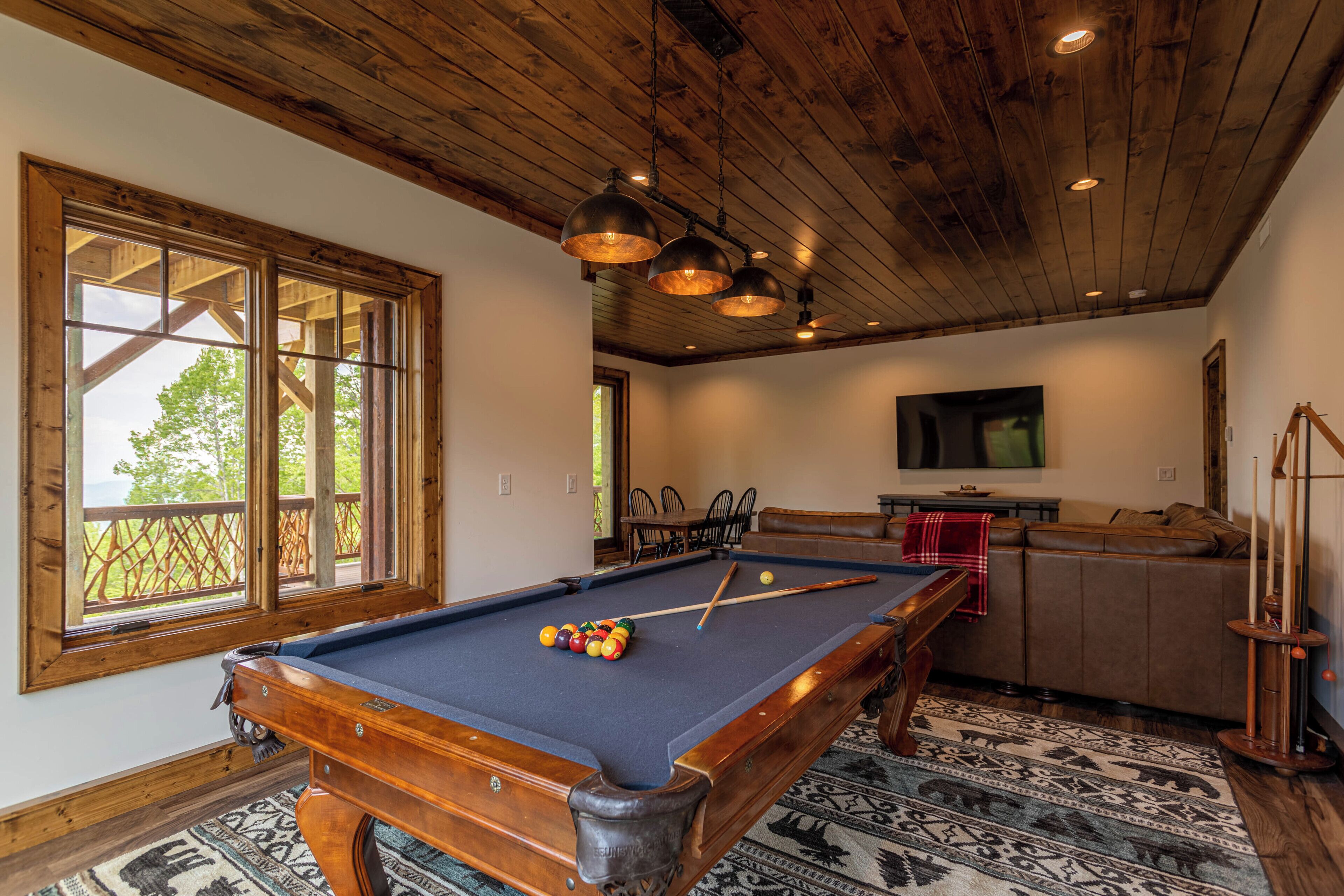 A pool table in a room with wooden ceilings and large windows.