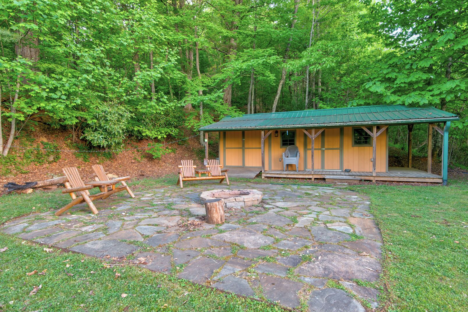 A rustic cabin with a stone patio, wooden chairs, and a fire pit.