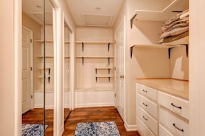 A narrow hallway with a wooden floor, a patterned rug, white storage units with shelves, and a white dresser with drawers. - Paws A While - Hot Tub, Pool Table, Firepit (Blowing Rock)