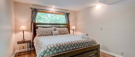 A bedroom with a wooden bed frame, a patterned bedspread, two bedside lamps, and a window with curtains.