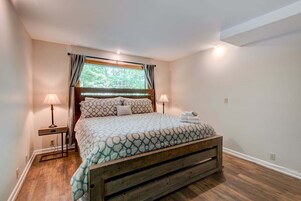 Un dormitorio con estructura de cama de madera, colcha estampada, dos lámparas de noche y una ventana con cortinas.
