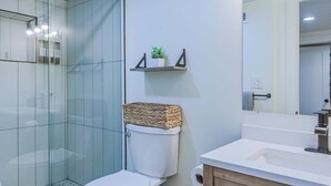 A modern bathroom with a glass shower enclosure, a white toilet, a wooden vanity with a mirror, and a small shelf with a plant. - 1409 #2 Sugar House (Salt Lake City)